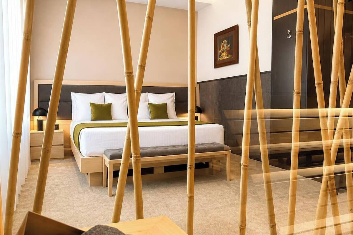 A room with a bed, bedside tables, a bench, and bamboo decor.