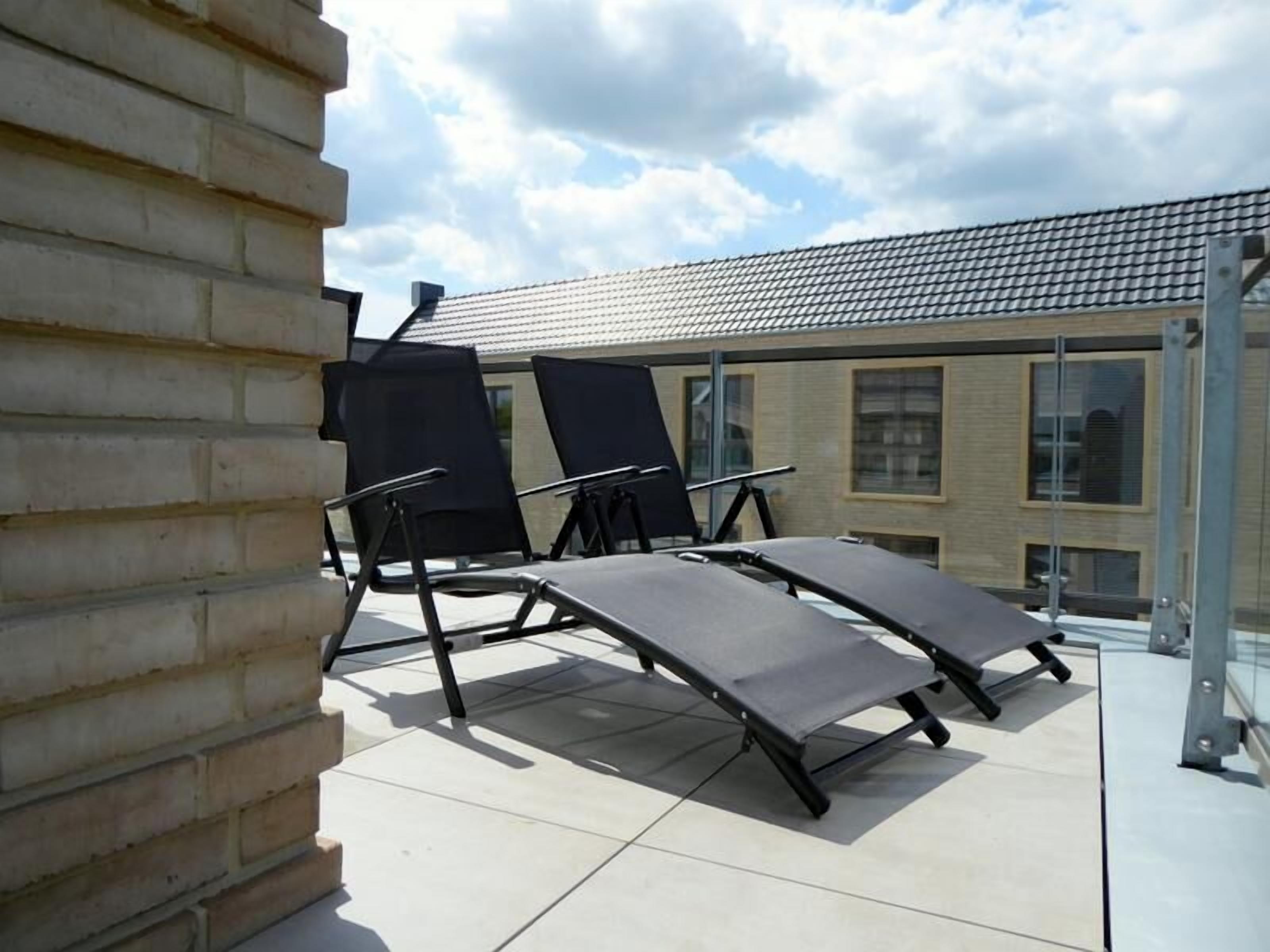 Una terrazza sul tetto con due poltrone e una ringhiera in vetro.