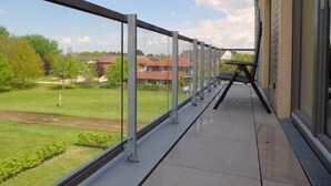 Un balcon doté d’une rambarde en métal, donnant sur un espace verdoyant et des bâtiments.