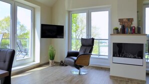Un salon moderne doté d’une cheminée, de grandes fenêtres, d’un téléviseur fixé au mur et d’un coin salon confortable.