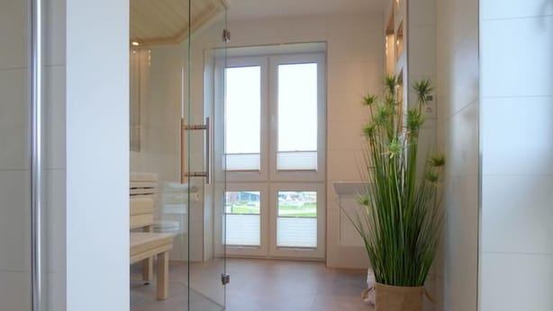 Une salle de bain moderne avec des portes en verre, un banc et une plante en pot.