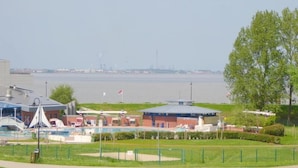 Une propriété située au bord de l’eau, dotée d’une piscine, d’un petit bâtiment avec un toit rouge et d’une zone herbeuse délimitée par une clôture.