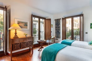 A hotel room with a wooden desk, a chair, a bed with two pillows, a window with a view of buildings, and a door with a sign. - Genteel Home Puerta Real (Seville)