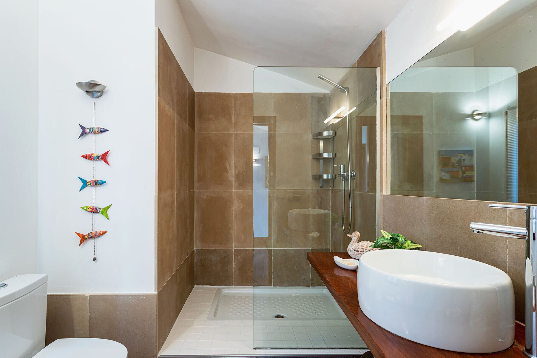 Un baño moderno con cabina de ducha de vidrio, un lavamanos blanco y decoración de peces en la pared.