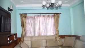 A living room with a sofa, television, and curtains. - Standard Rooms | Delights Home (Kathmandu)