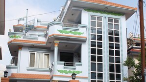 A multi-story residential building with a prominent balcony, a gated entrance, and a brick wall. - Standard Rooms | Delights Home (Kathmandu)