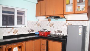 A kitchen with wooden cabinets, a refrigerator, a stove, and a window. - Standard Rooms | Delights Home (Kathmandu)