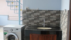 A compact kitchen with a washing machine, a sink, and a wooden cabinet. - Standard Rooms | Delights Home (Kathmandu)