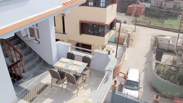 A rooftop terrace with a dining table and chairs, a staircase, and a parked car. - Standard Rooms | Delights Home (Kathmandu)