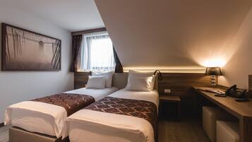 Quarto de hotel com duas camas, uma mesa, uma luminária e um quadro na parede.
