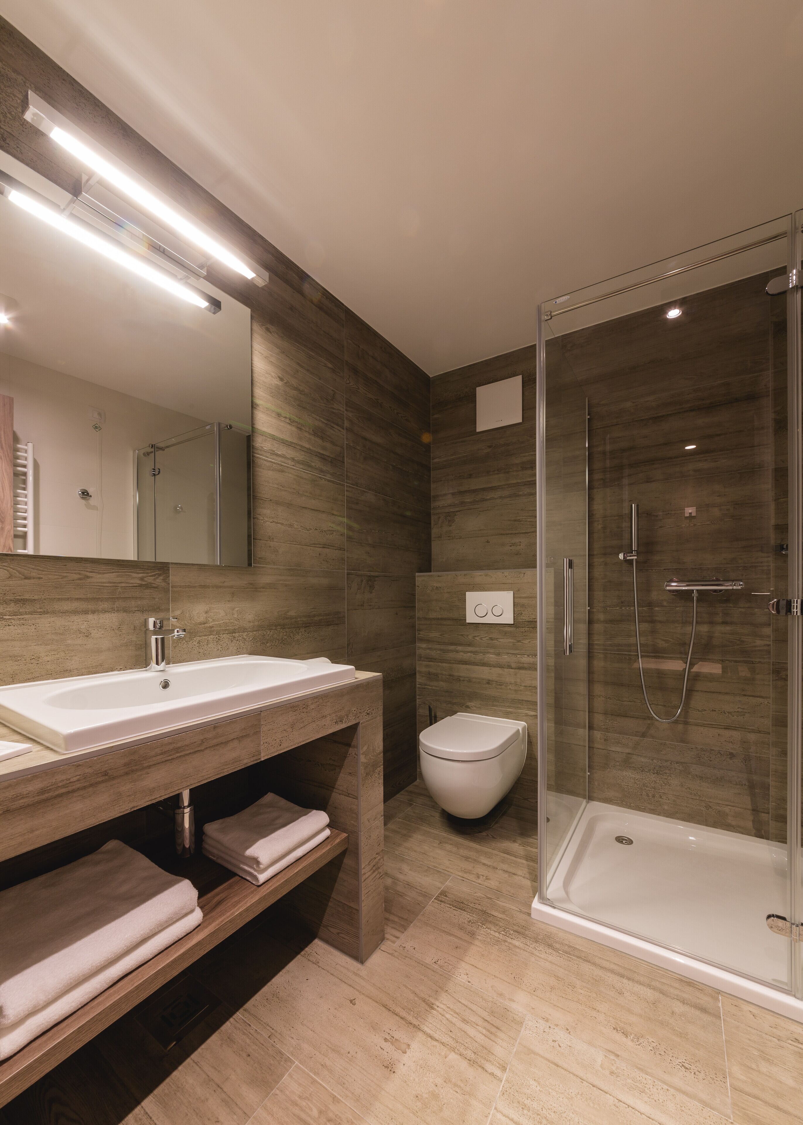 Un baño moderno con un espejo grande, un lavamanos, un inodoro y una ducha con mampara de vidrio.