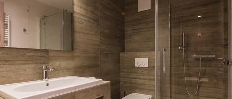 A modern bathroom with a large mirror, a sink, a toilet, and a glass-enclosed shower.