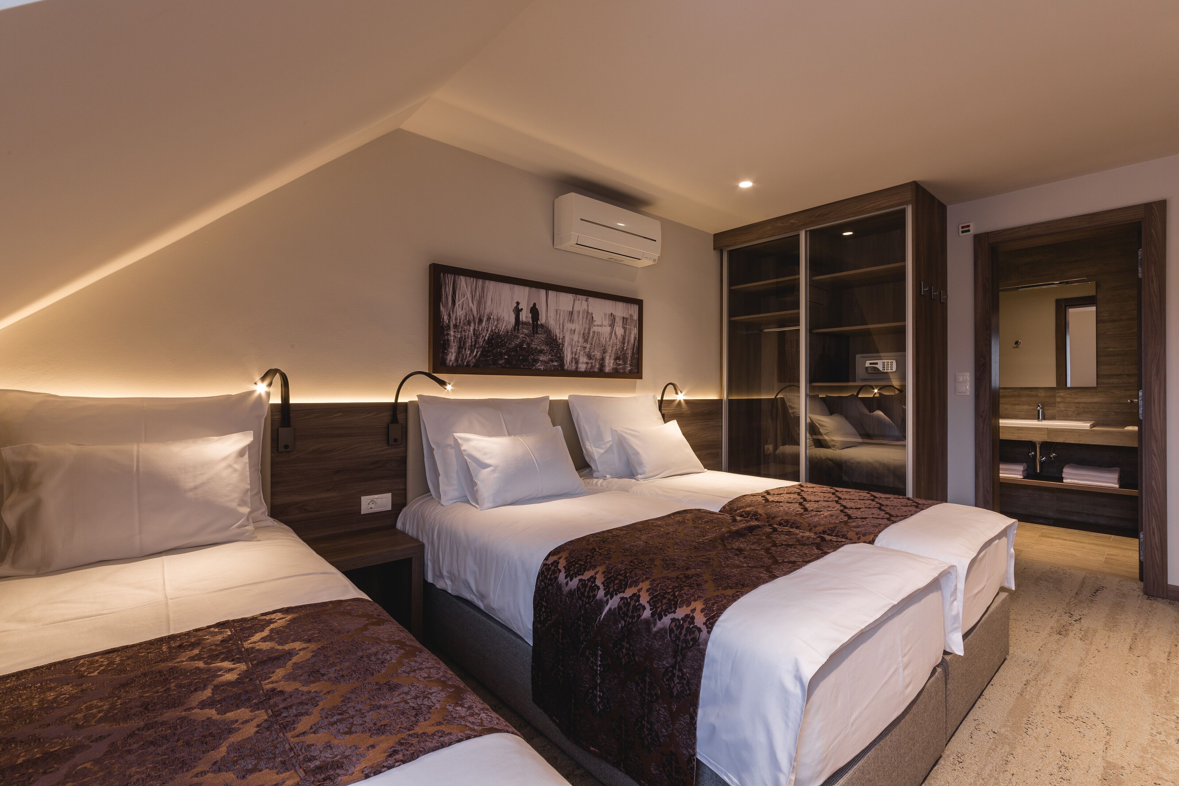 Una habitación de hotel con tres camas, un espejo grande y un armario con tocador integrado.