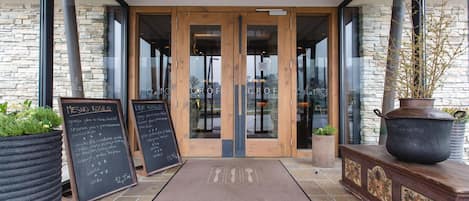 A restaurant entrance with a stone facade, wooden doors, and a chalkboard menu.