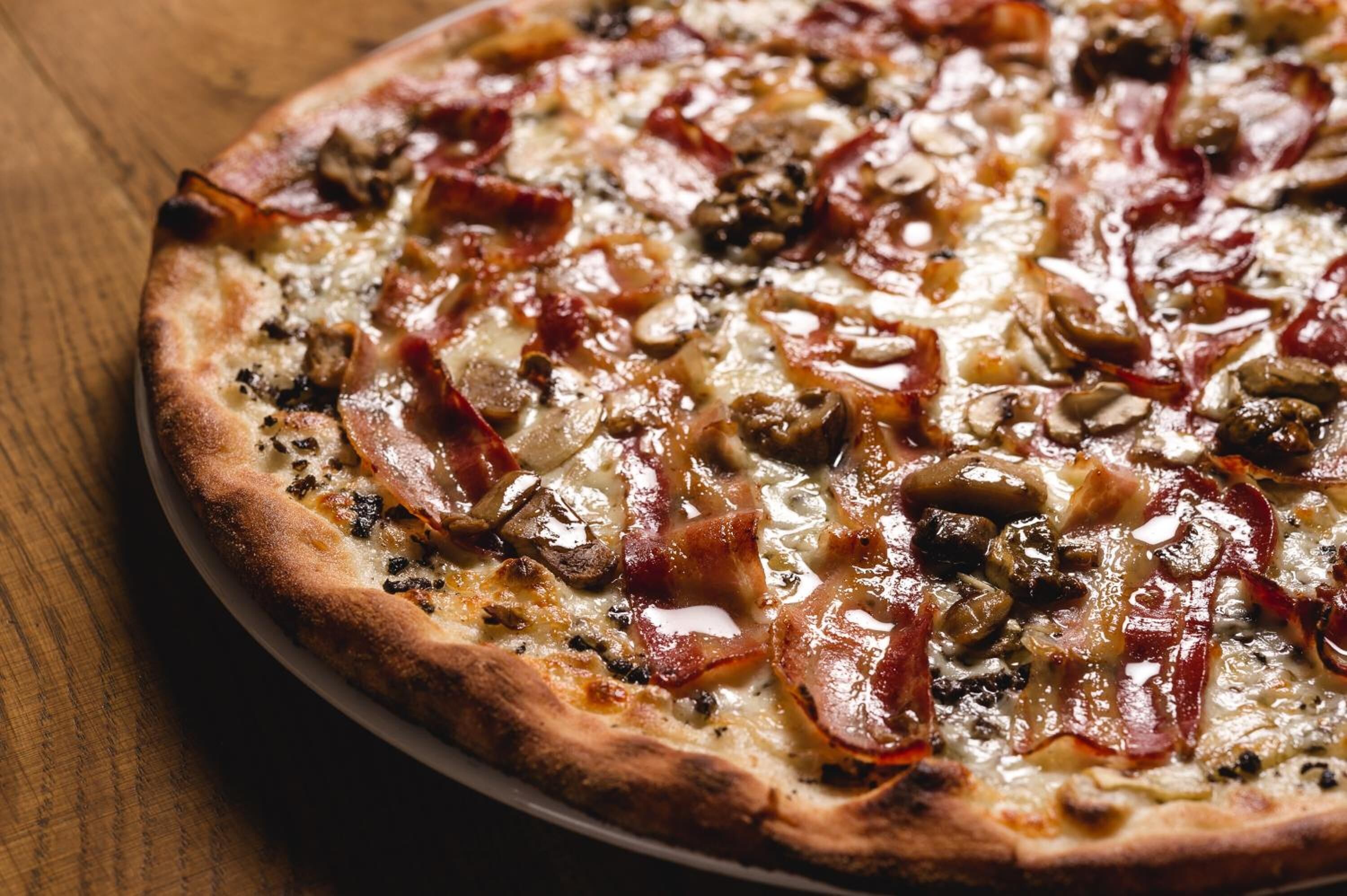 Une pizza avec des garnitures bien visibles, notamment du bacon et des champignons, posée sur une surface en bois.