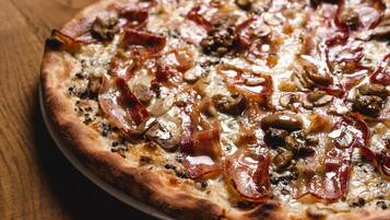Une pizza avec des garnitures bien visibles, notamment du bacon et des champignons, posée sur une surface en bois.