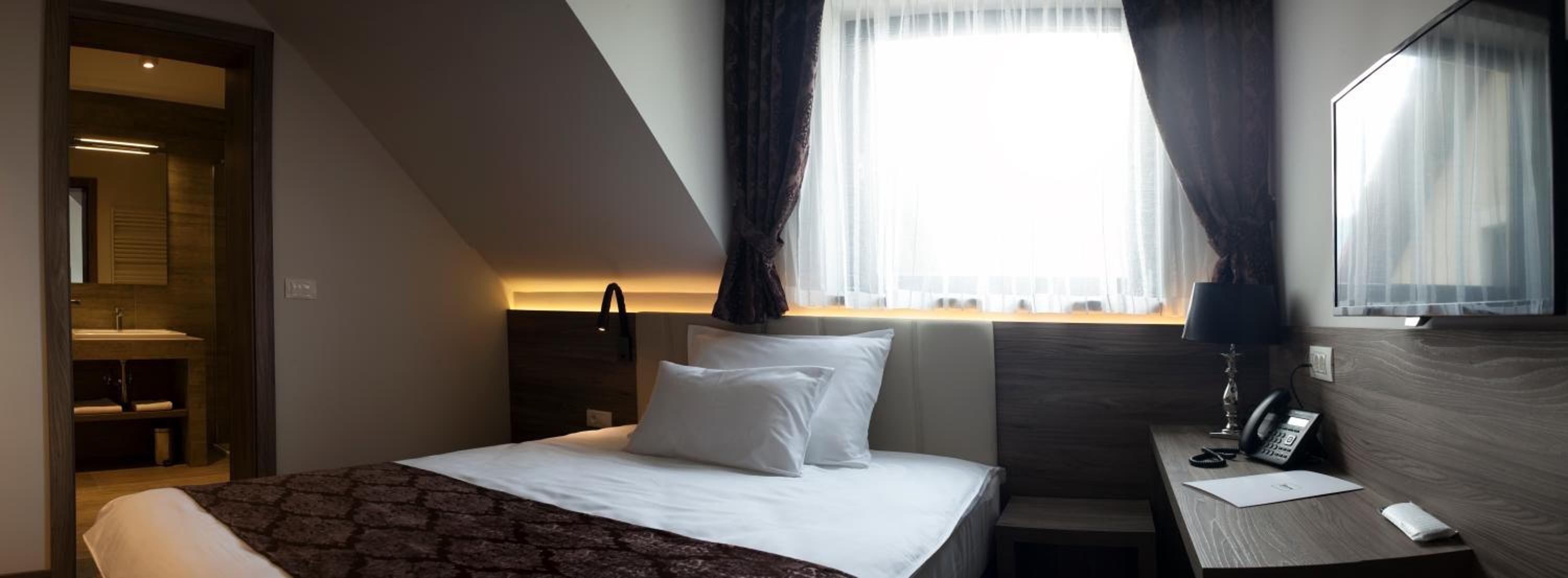 Une chambre d’hôtel moderne équipée d’un lit, d’une table de chevet et d’un bureau avec un téléphone.