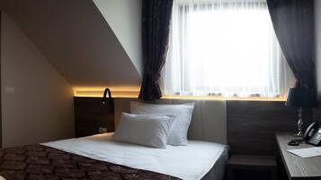 A modern hotel room with a bed, bedside table, and a desk with a phone.