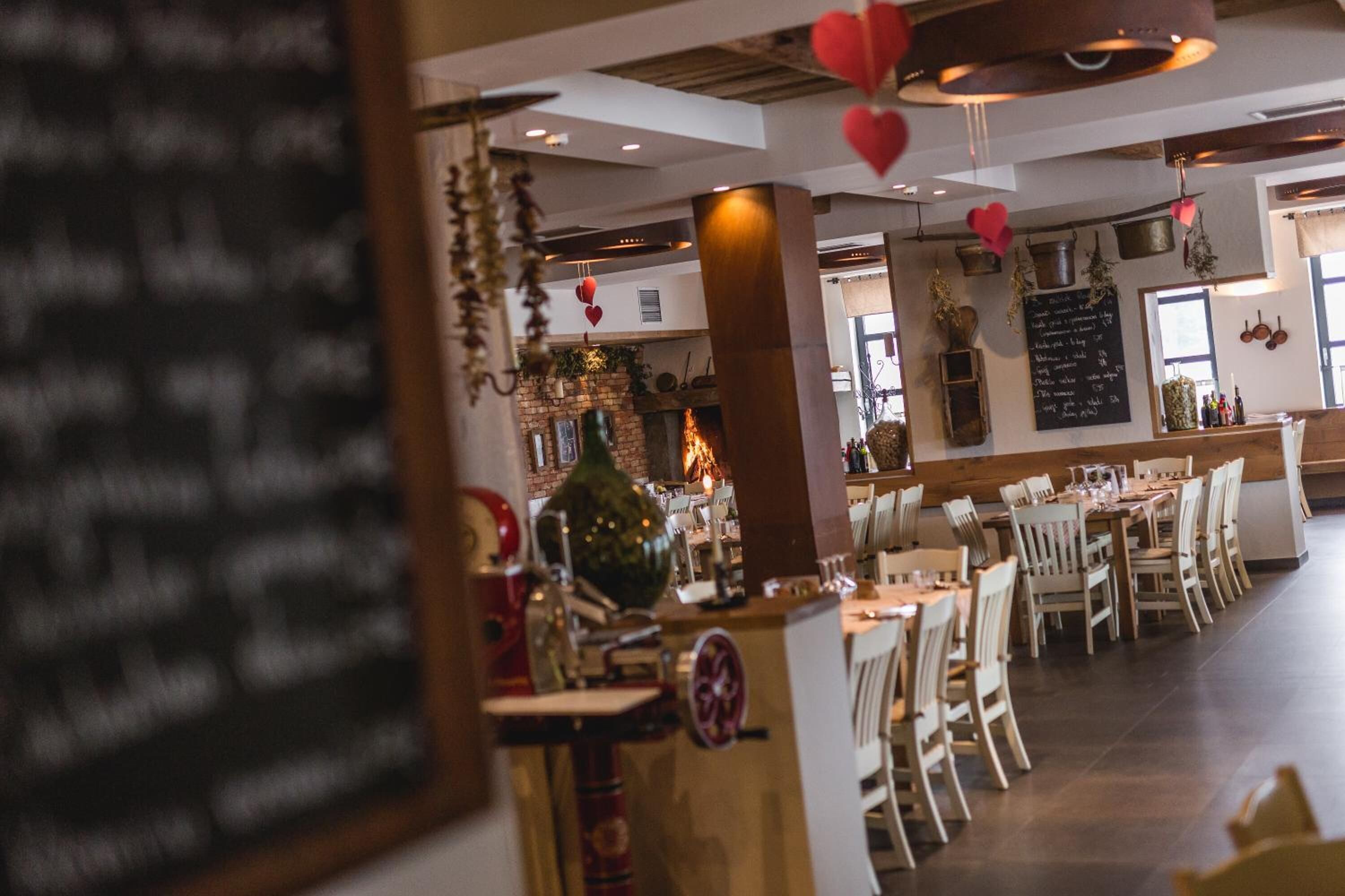 A restaurant with wooden tables and chairs, a brick fireplace, and hanging decorations.