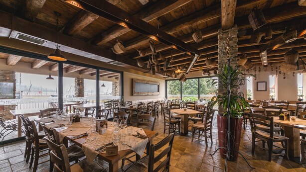 Un restaurante espacioso con mesas y sillas de madera, ventanas amplias y cestas colgantes.