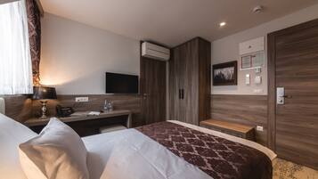 A hotel room with a bed, bedside table, lamp, air conditioning unit, and a wall-mounted TV.