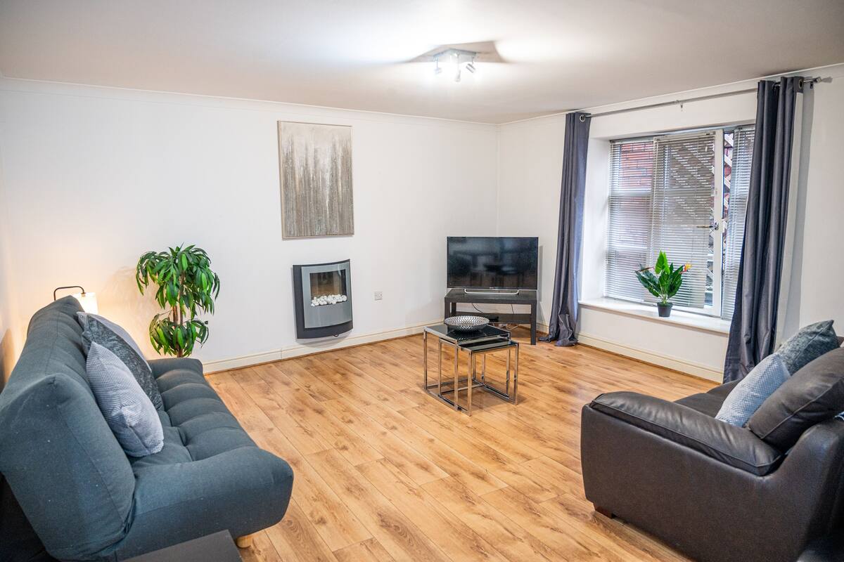 A modern living room with a grey sofa, a small coffee table, a flat-screen TV, and a potted plant.