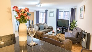 A modern living room with a sofa, a coffee table, a TV, and a vase with flowers. - The Bookbinders Residence Leeds City Centre (Leeds)