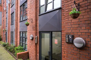 A brick building with a modern entrance, a doorbell, and a hanging basket with plants. - The Bookbinders Residence Leeds City Centre (Leeds)