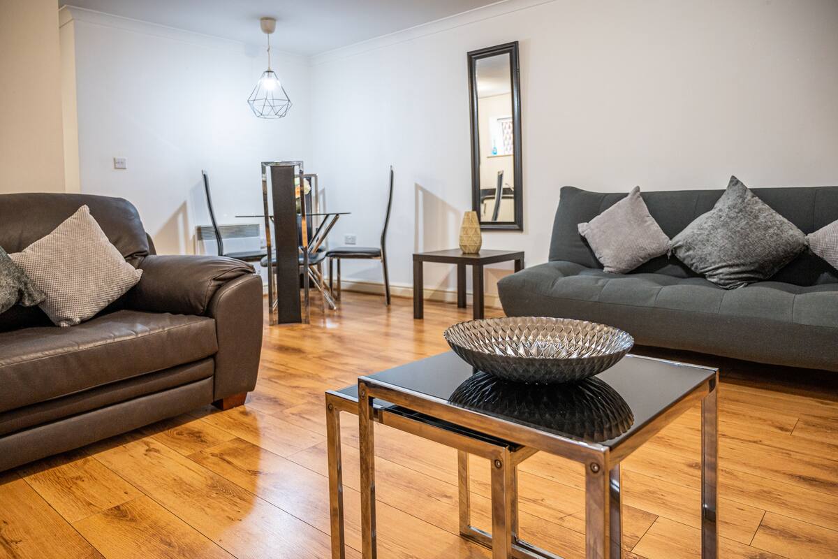 A modern living room with a leather sofa, a dark grey couch, and a black coffee table with a decorative bowl.