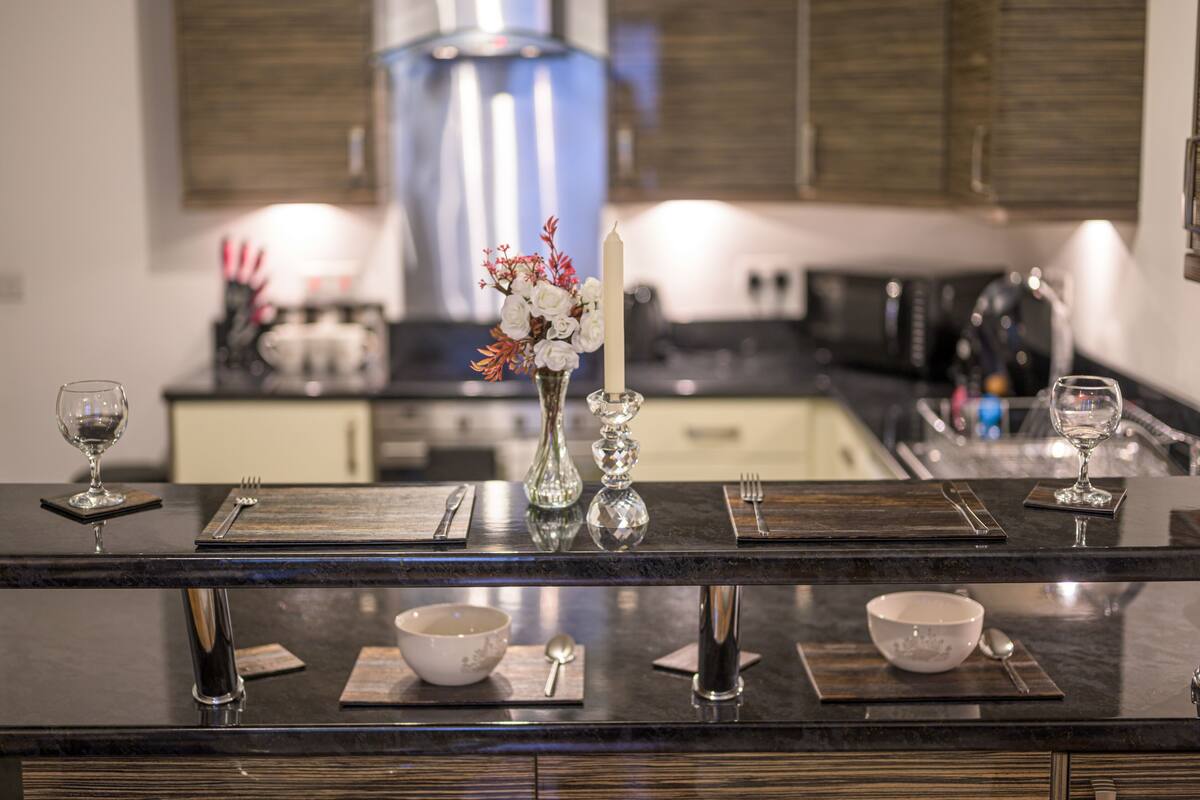 A modern kitchen with dark countertops, a central island with a candle, and a vase of flowers.