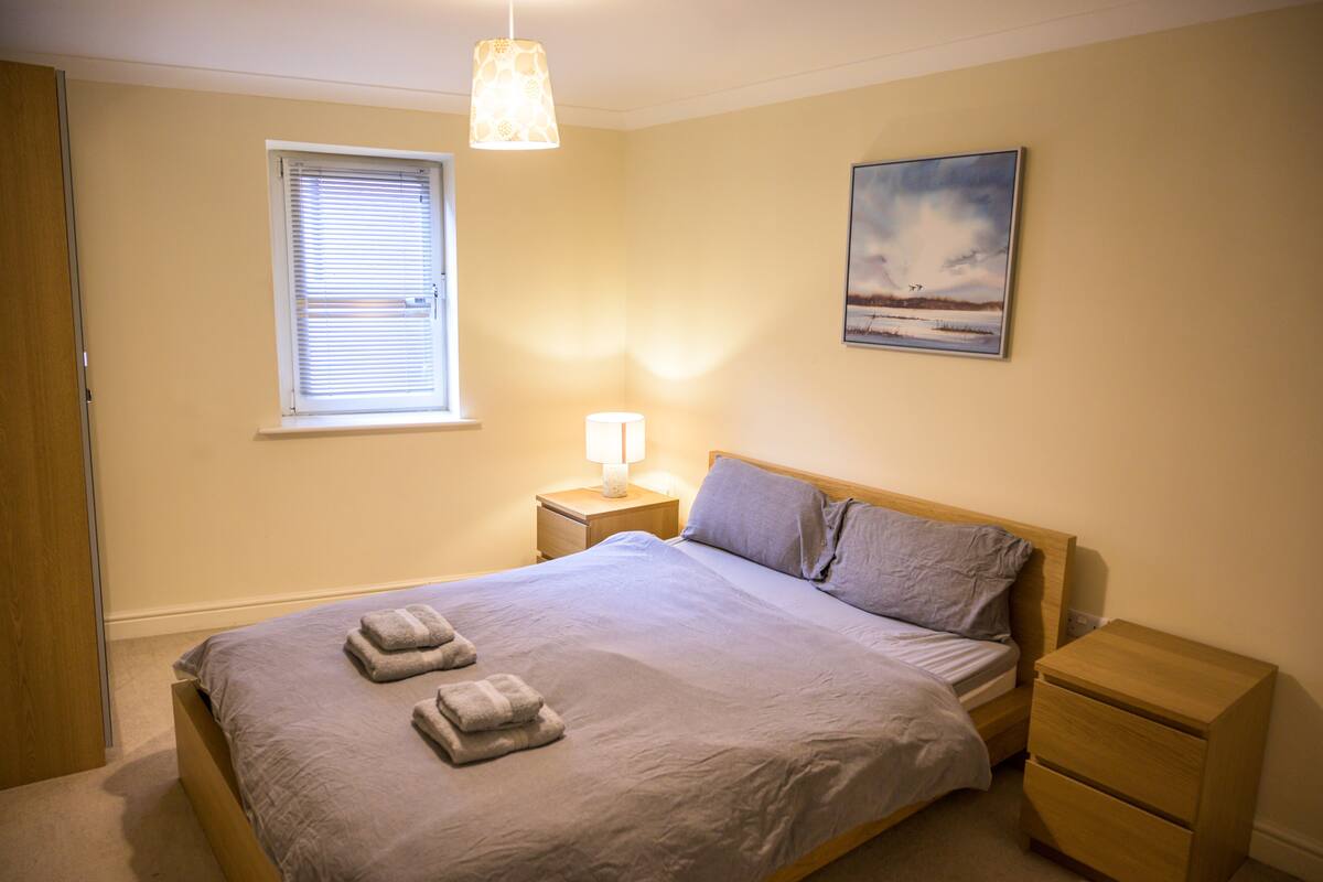 A bedroom with a bed, bedside tables, a window, and a painting on the wall.