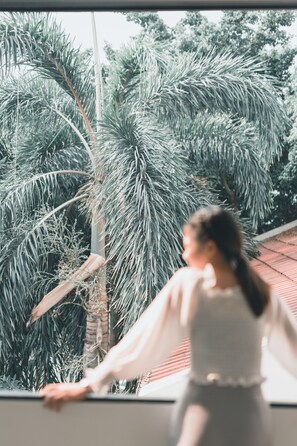 A person standing by a window with a view of palm trees and a red building. - 41Cafetel (Bangkok)