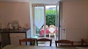 A hotel room with a bed, a desk with a sink, a chair, and a table with a red tablecloth. There is a view of an outdoor area with a table and chairs.