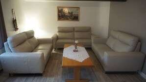 A living room with a beige sofa set, a wooden coffee table with a white cloth, and a painting on the wall.