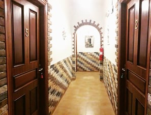 Un pasillo con puertas de madera numeradas 5 y 2, que conduce a una habitación con suelo de baldosas y un arco de ladrillo.