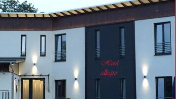 Fachada moderna de hotel con una entrada amplia, iluminación exterior y el nombre 'Hotel Allegro' exhibido en un lateral.