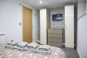 A bedroom with a bed, a wooden door, a wardrobe, a television, and a radiator. - V2 Residence (Leeds)
