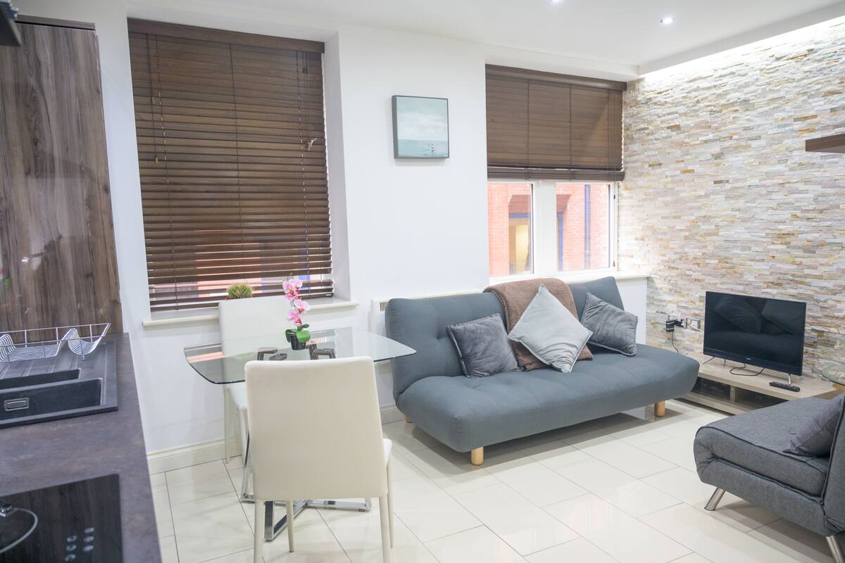 A modern living room with a grey sofa, a TV, and a stone wall.