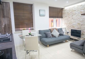 A modern living room with a grey sofa, a TV, and a stone wall. - V2 Residence (Leeds)