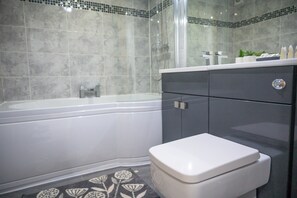 A modern bathroom with a bathtub, toilet, and vanity. - V2 Residence (Leeds)
