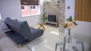 Una sala moderna con sofá, una mesita de centro de vidrio, televisor y pared de piedra.