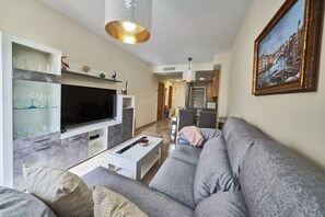 A modern living room with a grey sofa, a flat-screen TV, and a dining area with a table and chairs.