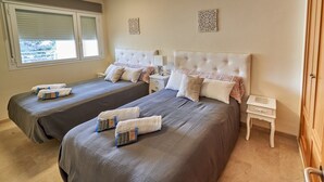 A hotel room with two beds, a small bedside table with a lamp, and a view of the outdoors through a window. - Beachfront apartment, with pool and urban areas. Zarati (Isla Cristina)
