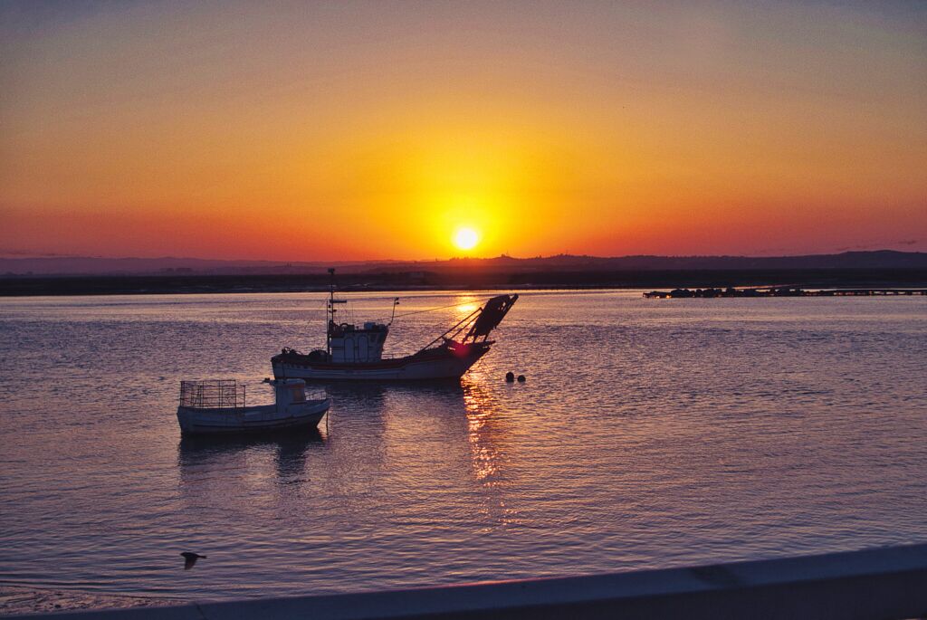 A sunset over a calm body of water with two boats anchored.