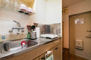 A kitchen with a stainless steel sink, a dish rack, a microwave, and a toilet paper holder. - Rooms Ropponmatsu (Fukuoka)