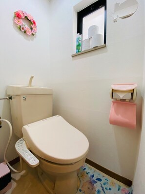 A bathroom with a toilet, a toilet paper holder, a hand dryer, and a small shelf with a mirror and a bottle. - Rooms Ropponmatsu (Fukuoka)