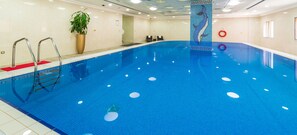 A large indoor swimming pool with clear blue water, a lifeguard stand, and a dolphin mosaic on the wall. - Al Diyafa Furnished Suites (Doha)