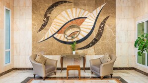 A lobby with a large wall mural, two armchairs, a small table, and a potted plant. - Al Diyafa Furnished Suites (Doha)