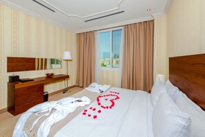 A hotel room with a large bed, a wooden headboard, a bedside table, a mirror, and a window with curtains. - Al Diyafa Furnished Suites (Doha)