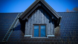 Un bâtiment doté d’un toit à forte pente, d’une lucarne et d’une échelle visible.